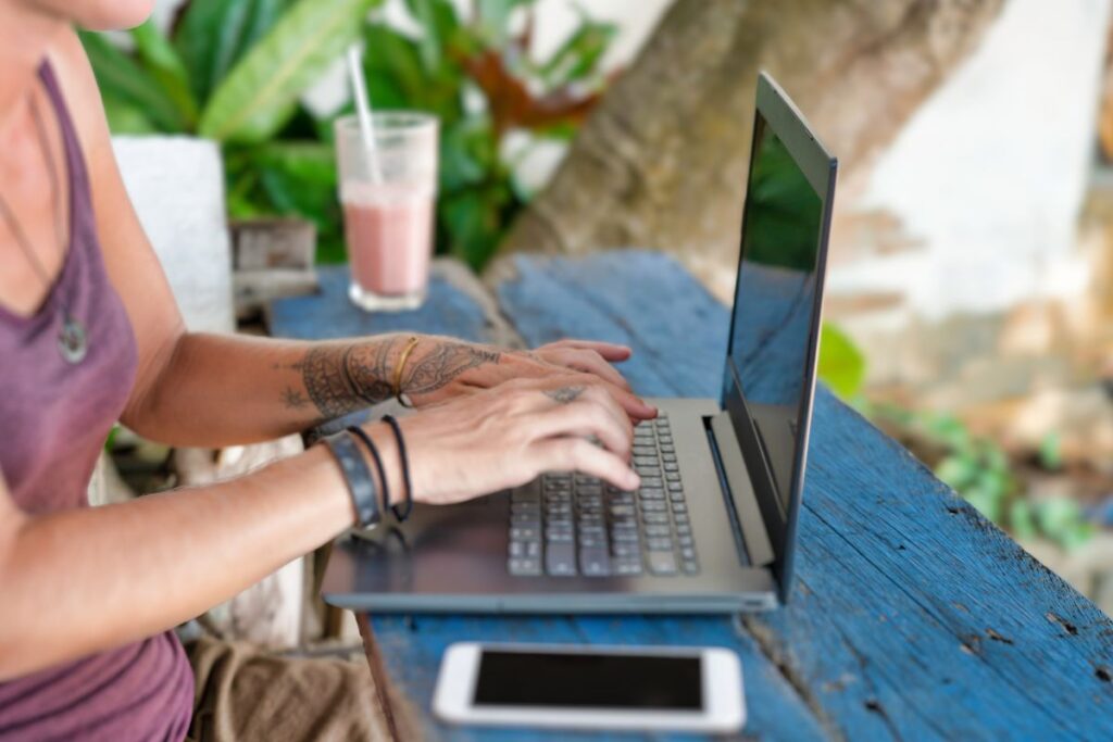 Person mit Tattoos arbeitet im Freien am Laptop – Kreative nutzen KI zur Automatisierung ihrer Arbeit